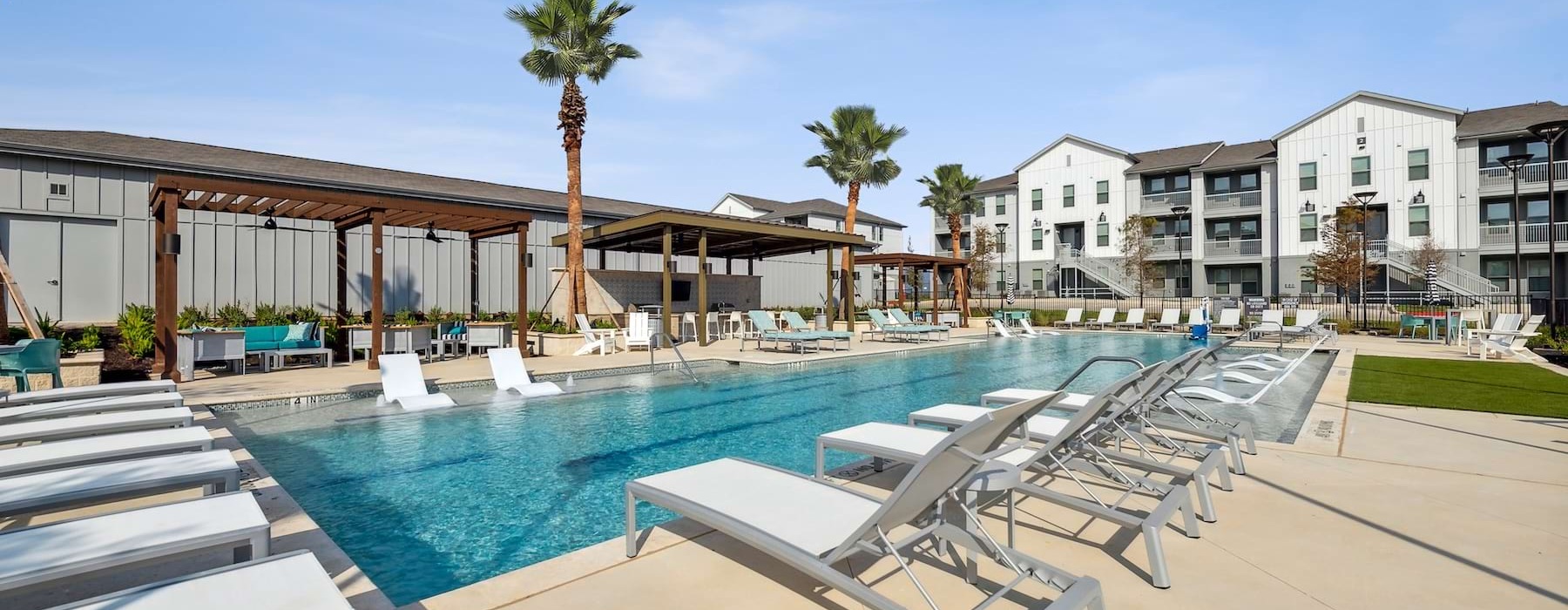 The pool area at Alta Trails Apartments for rent in Bastrop, TX, featuring lounge chairs and palm trees.